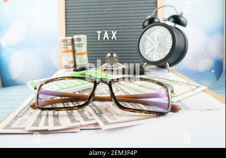 Concetto di riempimento delle tasse - ‘tempo di imposta’ wordss. Soldi falsi, penna, occhiali, lente d'ingrandimento e un orologio con la metà della forma IRS 1040 degli Stati Uniti. Foto Stock