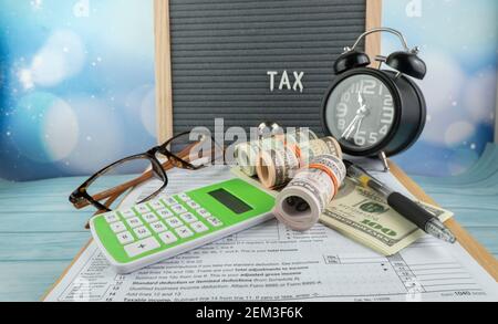 Concetto di riempimento delle tasse - ‘tempo di imposta’ wordss. Soldi falsi, penna, occhiali, lente d'ingrandimento e un orologio con la metà della forma IRS 1040 degli Stati Uniti. Foto Stock