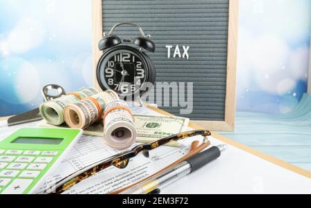 Concetto di riempimento delle tasse - ‘tempo di imposta’ wordss. Soldi falsi, penna, occhiali e un orologio che presenta la metà del modulo US IRS 1040. Foto Stock