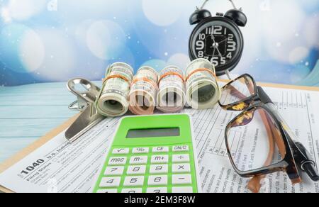 Concetto di riempimento delle tasse - ‘tempo di imposta’ wordss. Soldi falsi, penna, occhiali e un orologio che presenta la metà del modulo US IRS 1040. Foto Stock