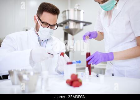 Lavoratore di laboratorio protetto che esegue un test con liquido rosso e fragola con una siringa. Foto Stock