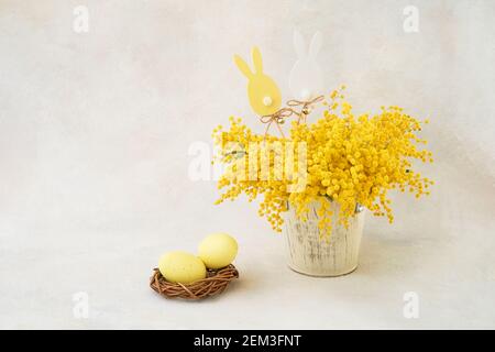 Uova di Pasqua e mimosa fiori bouquet in un vaso su uno sfondo chiaro. Concetto di Pasqua. Spazio di copia per il testo Foto Stock