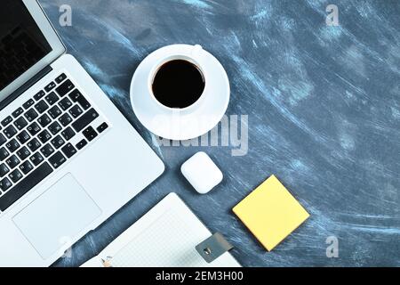 Una tazza di tè, computer portatile, notebook, bicchieri e appunti sulla scrivania blu Foto Stock