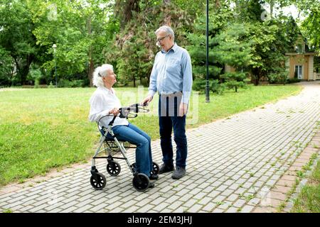 L'uomo anziano amorevole che tiene la compagnia alla sua moglie amorevole dentro il parco mentre la aiuta a guadagnare la sicurezza di camminare Foto Stock
