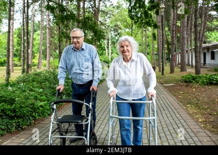 Coppia senior che cammina nel parco con l'aiuto di assistenti di camminare Foto Stock