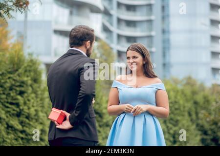 Uomo nascondendo dono dietro la schiena e sorridente donna Foto Stock