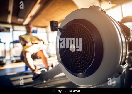 Primo piano della vista di messa a fuoco della macchina, con una forte motivazione e. uomo bodybuilder calvo muscolare mirato con auricolari che tira la barra nella moderna e soleggiata palestra Foto Stock