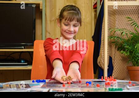 Una ragazza lancia grandi dadi facendo un'altra mossa mentre si gioca un gioco da tavolo al tavolo Foto Stock