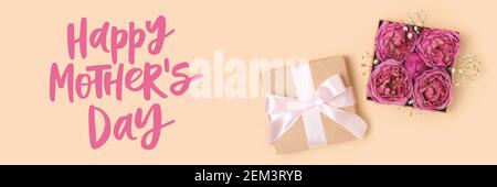 Banner con confezione regalo aperta con fiori di rosa all'interno. Happy Mothers Day citazione su sfondo beige. Foto Stock