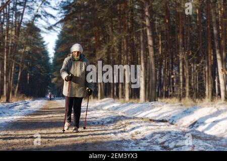 Attiva una donna anziana impegnata nel nordic walking con bastoni nella foresta invernale Foto Stock