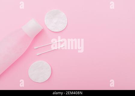 Composizione semplice con lozione in bottiglia di plastica, tamponi e bastoni di cotone su sfondo rosa, vista dall'alto, layout Foto Stock