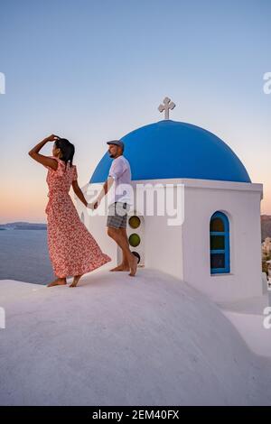 Santorini Grecia, giovane coppia di mezza età europea e asiatica in vacanza al villaggio greco di Oia Santorini Grecia, vacanza di lusso Santorini. Uomo e donna di mezza età guardando tramonto Santorini Foto Stock