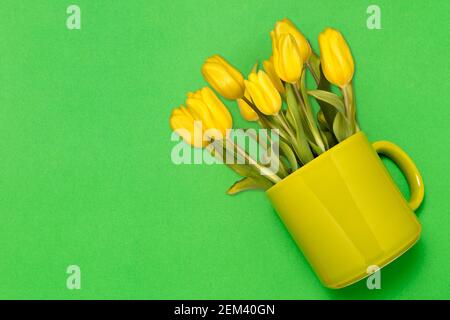 Layout creativo fatto di caffè o tazza da tè con il giallo tulipani su sfondo verde Foto Stock