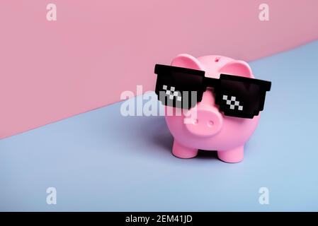 Rosa piggy banca di denaro con occhiali da sole neri su rosa e. sfondo blu Foto Stock