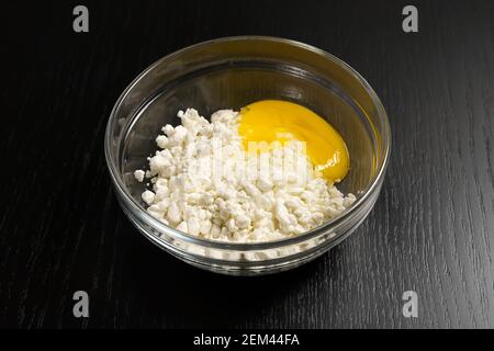 Formaggio di cottage granuloso, uovo in una ciotola di vetro su un tavolo nero primo piano Foto Stock