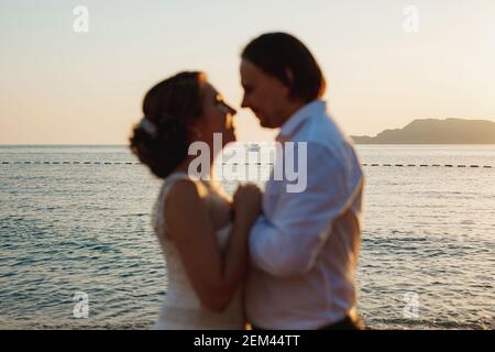 La sposa e lo sposo si abbracciano sulla pittoresca riva del mare, coppia offuscata Foto Stock