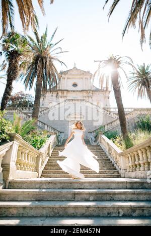 Una sposa in un abito da sposa vortica sull'antica scalinata di un tempio a Prcanj, la sua gonna flutters nel vento Foto Stock