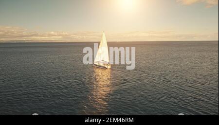 Aereo di yacht che naviga in acque oceaniche al sole con le nuvole. Barca a vela bianca in mare aperto. Vacanze estive a vela. Mare sereno con trasporto in acqua. Relax cinematografico e tranquillo paesaggio acquatico Foto Stock