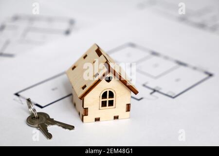 Modello di casa in legno e chiavi sullo sfondo della pianta dell'appartamento. Disegno di casa, acquisto di beni immobili Foto Stock