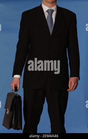 Uomo d'affari bianco senza volto in un vestito nero con un cravatta blu con borsa portadocumenti in pelle nera contro il blu sfondo Foto Stock