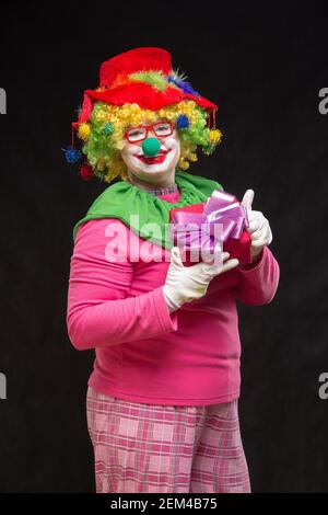 Funny clown con shaggy capelli e un allegro make-up tenendo un dono Foto Stock