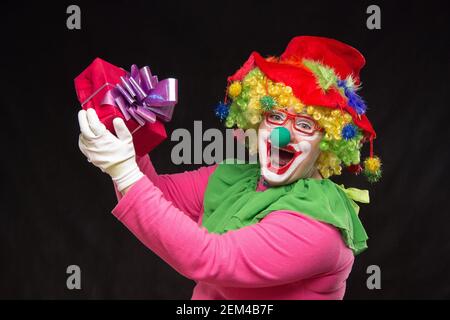 Funny clown con shaggy capelli e un allegro make-up tenendo un dono Foto Stock