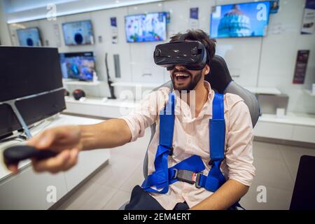 Primo piano di messa a fuoco di soddisfatto emozionato felice sorridente giovane lo studente ha sopportato un uomo che teneva il joystick wireless in mano mentre Test degli occhiali di protezione VR in una t Foto Stock
