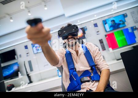 Primo piano ritratto di soddisfatto emozionato felice sorridente giovane lo studente ha sopportato un uomo che teneva il joystick wireless in mano mentre Test degli occhiali di protezione VR e. Foto Stock