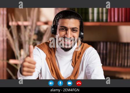Sorridente uomo in cuffia che ha una lezione online, mostrando il pollice in su Foto Stock