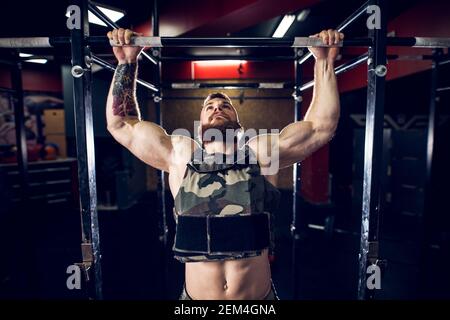 Ritratto primo piano di forte motivata e focalizzata muscolosa bearded corto capello bodybuilder uomo che fa tirare su la barra nella palestra scura. Foto Stock