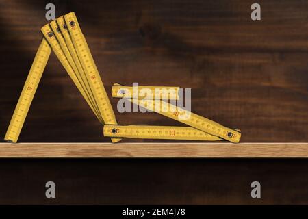 Primo piano di un vecchio righello pieghevole in legno giallo, metro, unità di lunghezza. Sopra una mensola di legno. Fotografia. Foto Stock