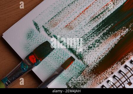Due pennelli, carta, tratti di vernice arancione e verde mescolati sulla carta, primo piano Foto Stock