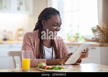 Giovane donna nera sorridente che usa Digital Tablet durante la colazione in Cucina Foto Stock