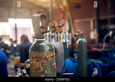 Primo piano della vista di messa a fuoco dell'attrezzatura di saldatura. Serbatoio per bombola di gas acetilene con manometri regolatori di misura nell'officina di tessuti industriali. Foto Stock