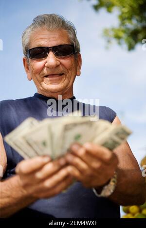 Primo piano di un uomo anziano che conta le fatture del dollaro americano e. sorridente Foto Stock