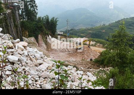 Terreno di scavo dell'escavatore. Cantiere con macchinari pesanti. Grande pila di pietre e ghiaia. Splendida vista sulla valle e sulle montagne Foto Stock