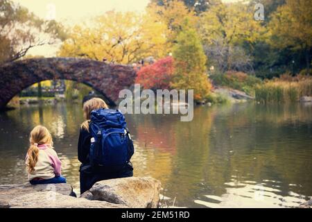 Vista posteriore di una ragazza e una donna seduta sulle rocce lungo un fiume e la città di New York, nello Stato di New York, Stati Uniti d'America Foto Stock
