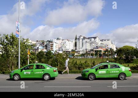 Da Lat, Vietnam - Luglio, 2015: Due simili taxi auto verdi sulla strada e l'uomo che cammina tra di loro. Concetto di colore verde. Vista laterale Foto Stock