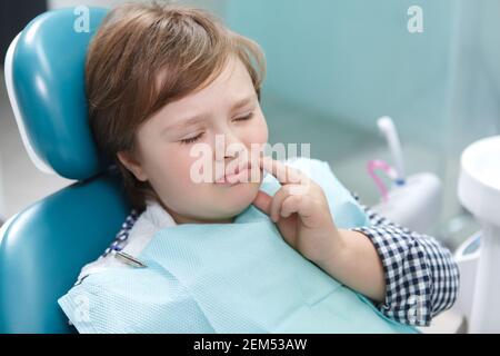 Primo piano di un ragazzo che ha mal di denti, seduto in sedia dentale presso l'ufficio dei dentisti Foto Stock