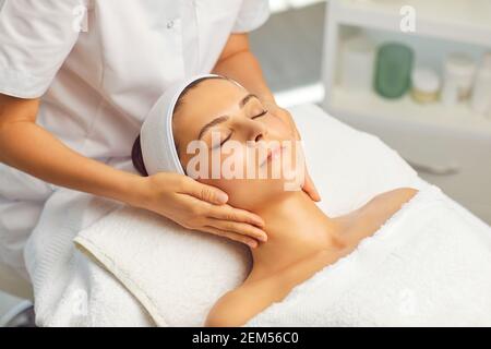 Mani di cosmetologist che fanno il massaggio manuale rilassante ringiovanente del viso per giovane donna Foto Stock