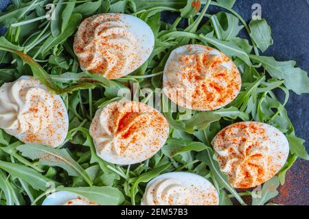 Uova divorate al keto con ripieno cremoso e paprika affumicata servita con insalata di rucola fresca, antipasto o finger food, tavolo da pranzo di Pasqua, primo piano, dir Foto Stock