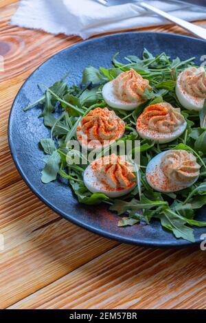 Uova keto divorate con ripieno cremoso e paprika affumicata servita con insalata di rucola fresca, antipasto o finger food, tavolo da pranzo di Pasqua, primo piano Foto Stock