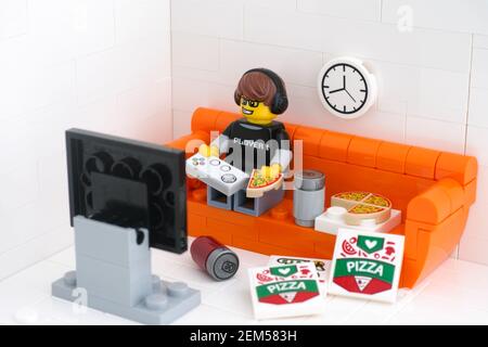 Tambov, Federazione Russa - 24 febbraio 2021 Lego video game minifigura ragazzo seduto su un divano giocando video giochi e mangiando pizza. Foto Stock