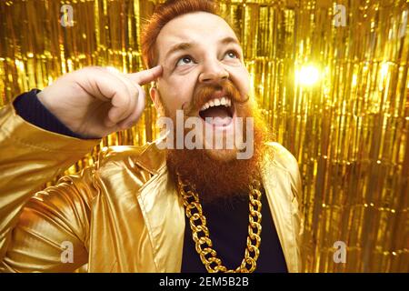 Un uomo dal braccio eccitato in un outfit stravagante con collana con catena in oro divertirsi in una festa Foto Stock