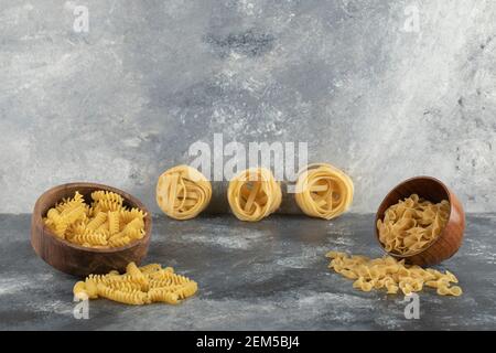 Vari tipi di pasta cruda in ciotole di legno Foto Stock
