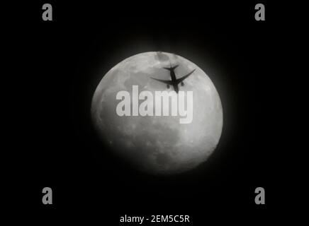 Wimbledon, Londra, Regno Unito. 24 febbraio 2021. Un volo serale di carico a lunga distanza attraversa la luna frizzante sopra Londra. L'AeroLogic Boeing 777 che vola nella stratosfera attraversa una Luna gibbosa al 90% di ceretta illuminata attraverso l'alta nube, diretta a Bruxelles da Cincinnati. Credit: Malcolm Park/Alamy Live News Foto Stock