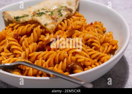 Fusilli in salsa di pomodoro con pane all'aglio in una ciotola. Sfondo concreto Foto Stock