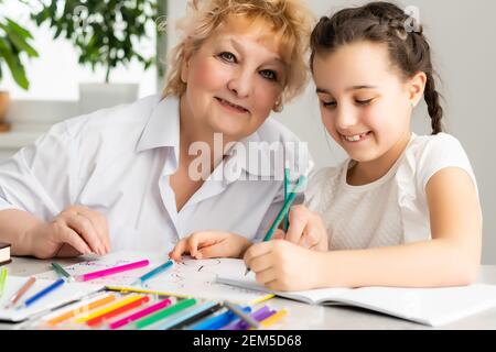 Felice nipote con nonna che si diverte, disegnando matite colorate, sedendosi insieme a casa, ridendo ragazza prescolare con sorridente pittura nonna Foto Stock