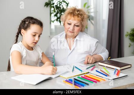 Felice nipote con nonna che si diverte, disegnando matite colorate, sedendosi insieme a casa, ridendo ragazza prescolare con sorridente pittura nonna Foto Stock