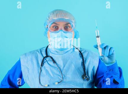 Medico in tuta protettiva, occhiali e maschera medica con siringa. Infermiere di sesso maschile che prepara l'iniezione con il vaccino. Foto Stock